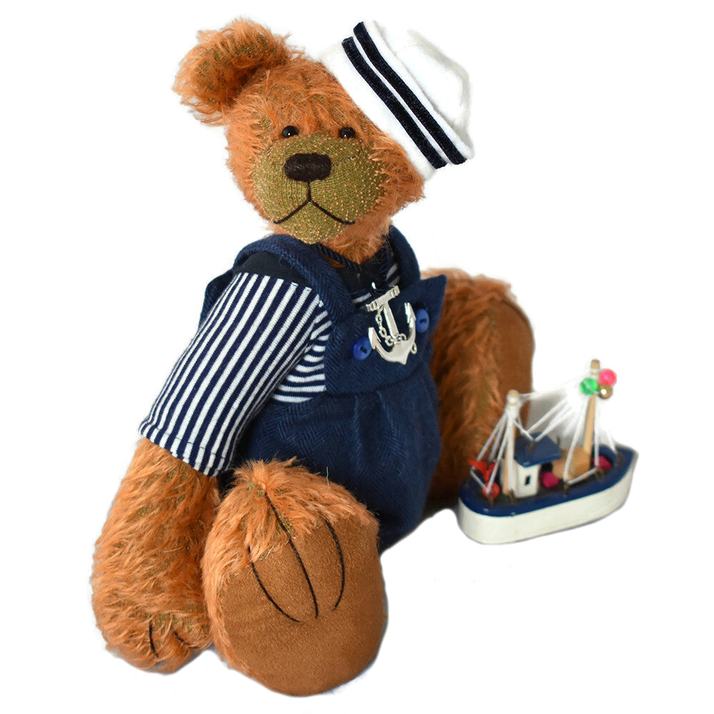 Handcrafted teddy bear in a nautical outfit with a small model ship on a white background